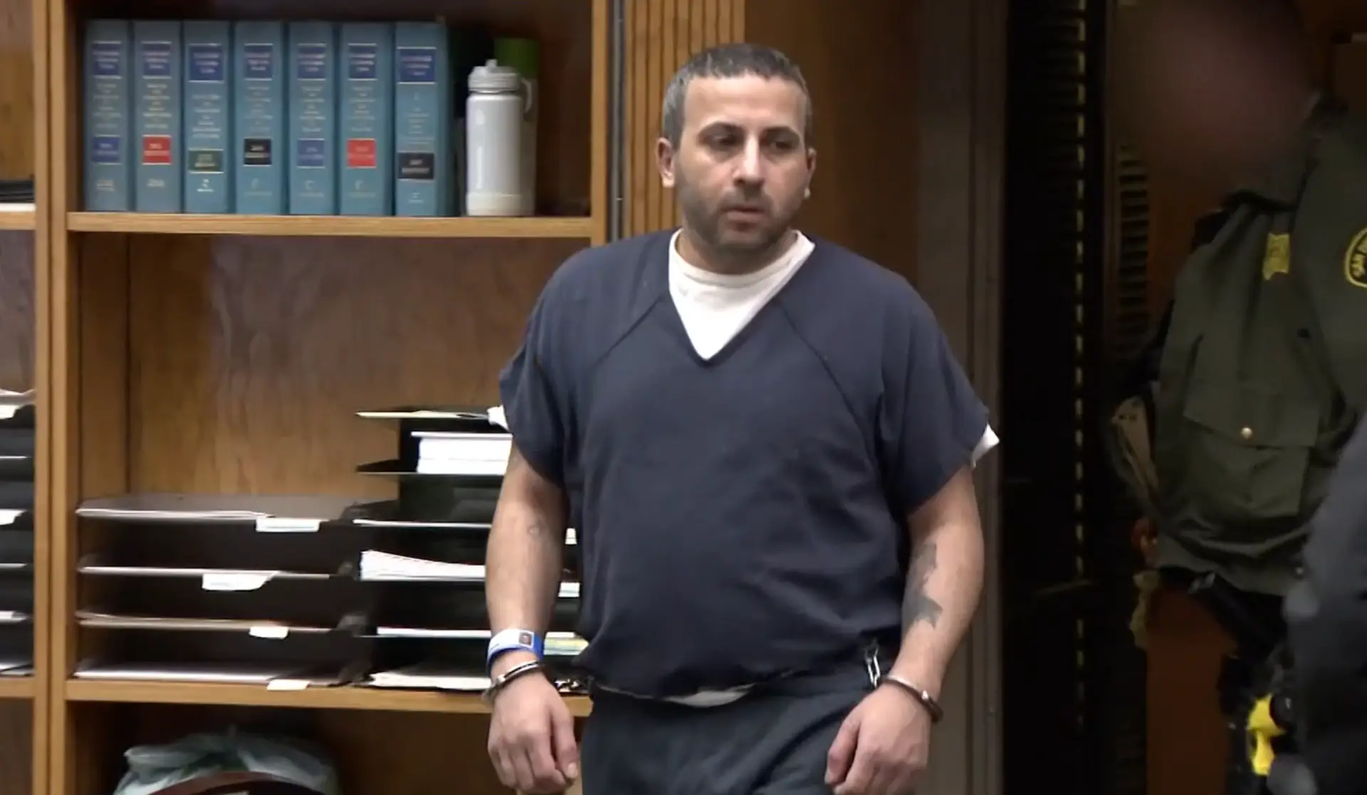 Man in jail clothing and handcuffs stands in a courtroom during a sentencing hearing.